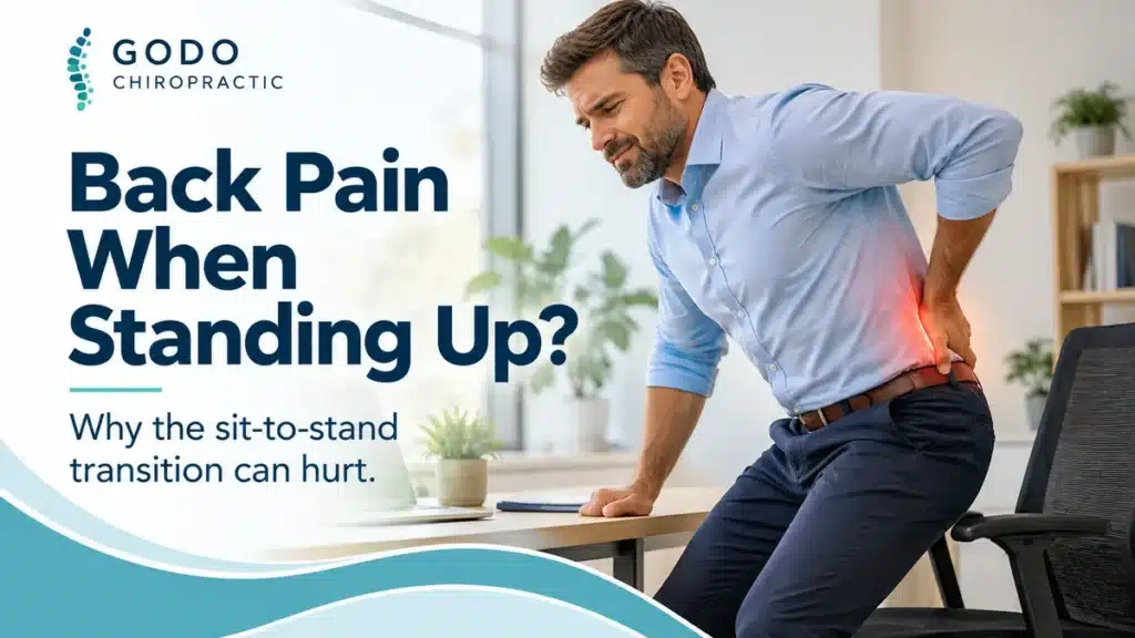 Man with lower back pain standing up from an office chair – Godo Chiropractic